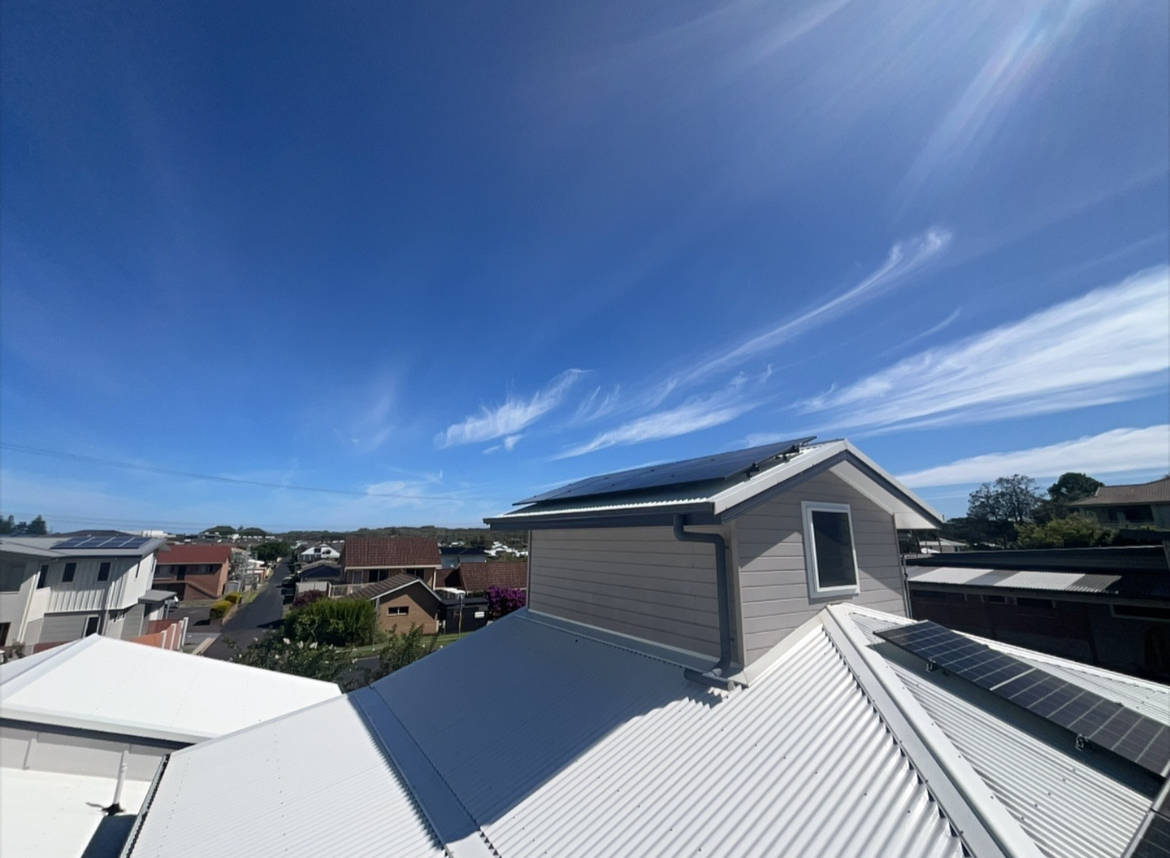 Solar panels on a Coffs Harbour rooftop with a clear blue sky and coastal suburb view
